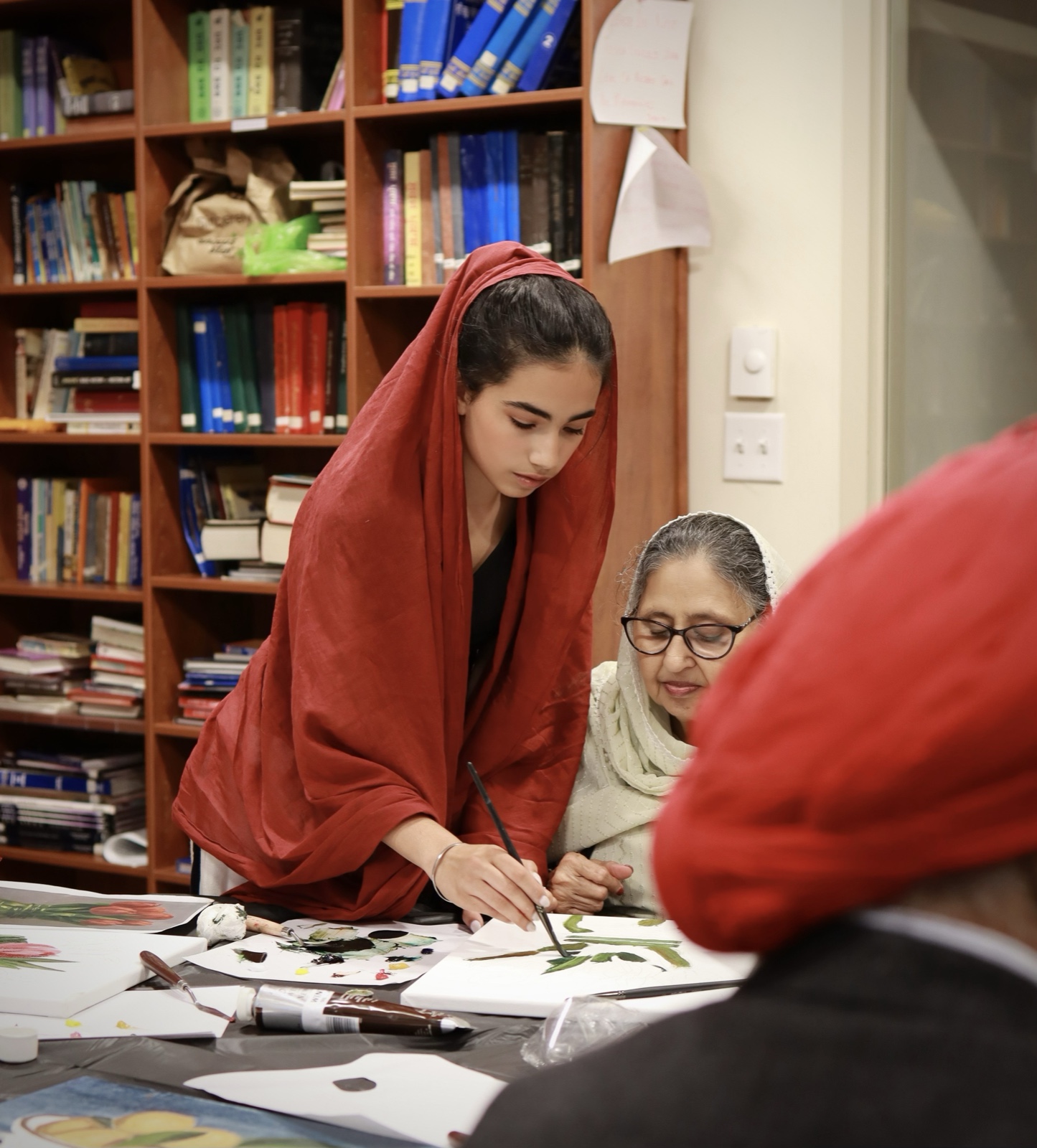 Parnaz leaning over to help a student with her painting