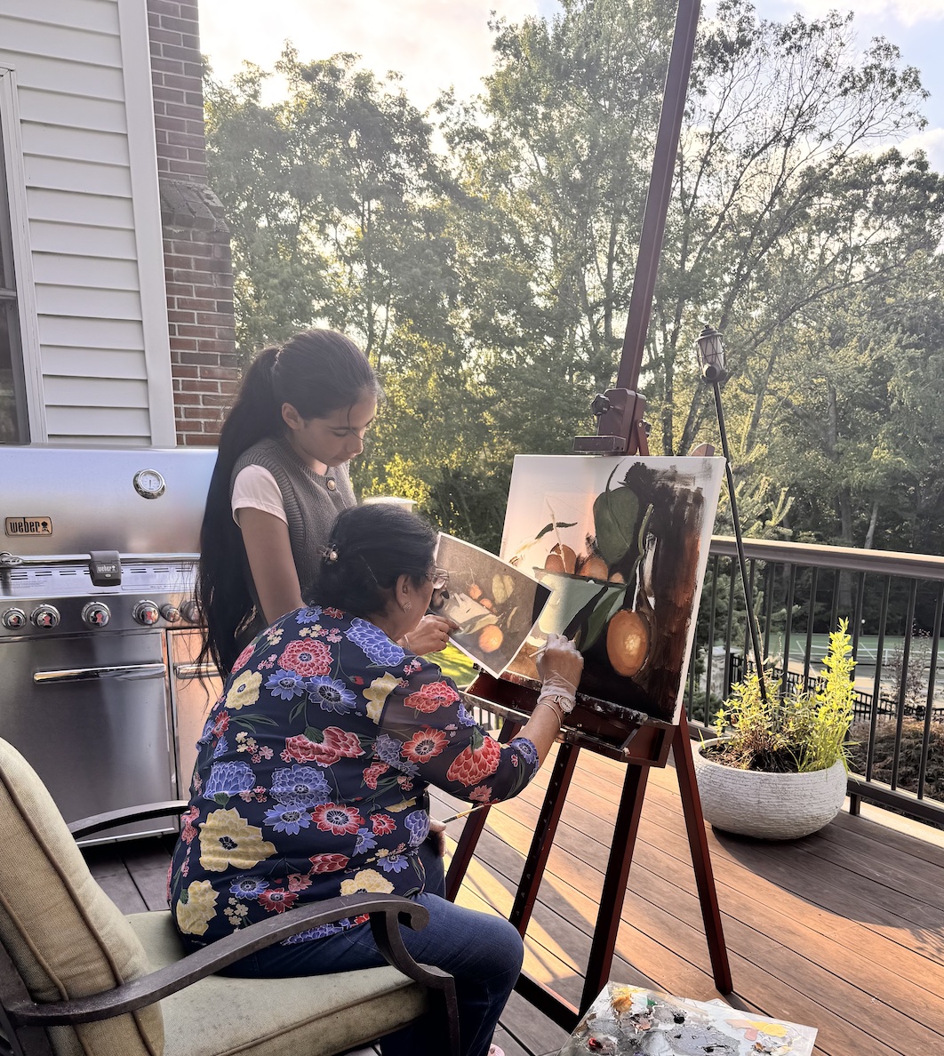 A student and her granddaughter painting a still life of oranges on the deck