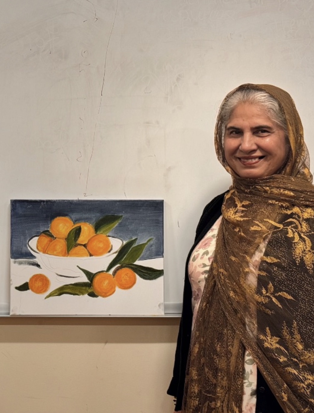 A student smiling next to her finished painting of oranges