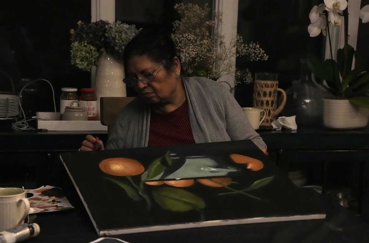 A student painting tulips at an easel by the window